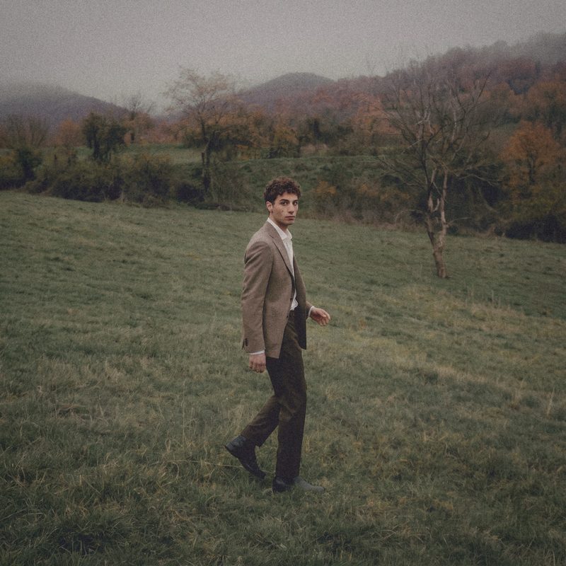 A man in a taupe jacket walks across a foggy meadow.